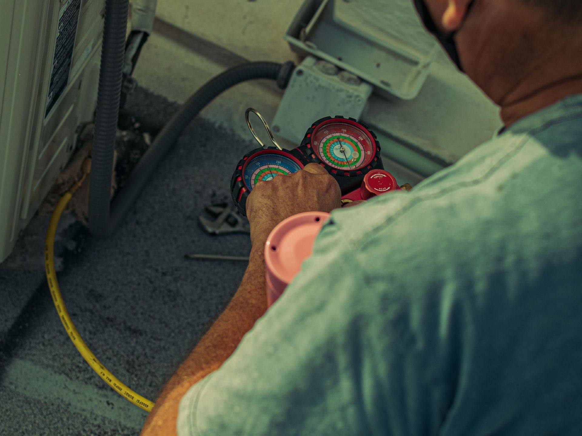 Professional technician repairing an outdoor air conditioning unit with gauges and tools.